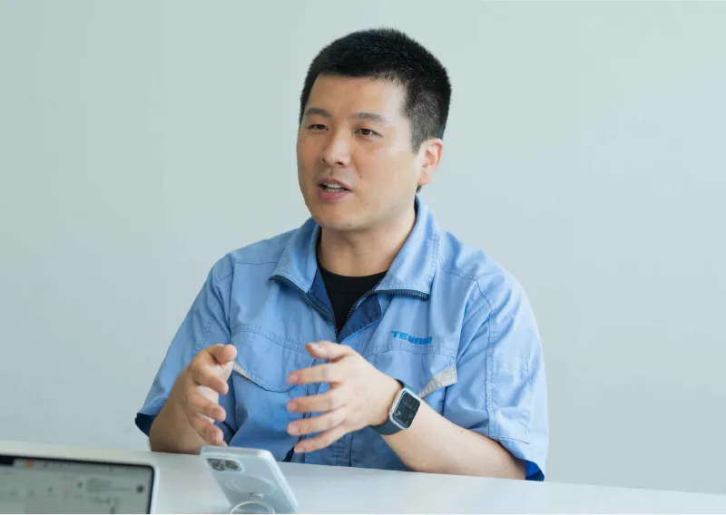 デスクに座り、身振り手振りを交えながら話すR.Mさん
