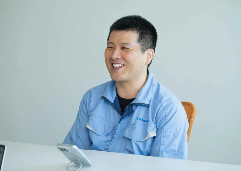 デスクに座り、笑顔を見せながら話すR.Mさん