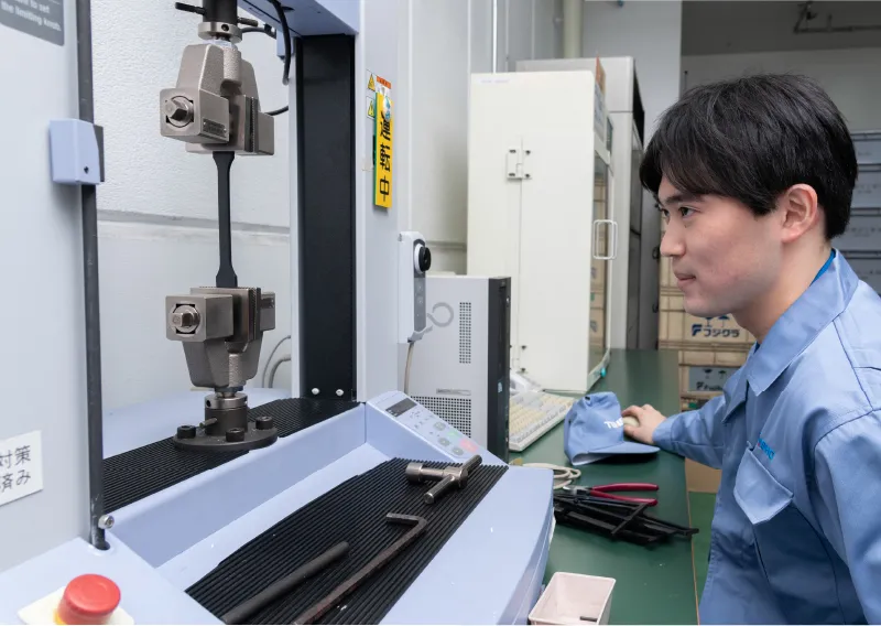 工場内で試験機を操作しながら、作業の様子を見つめるK.Kさん
