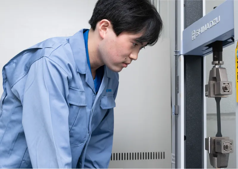 工場内で試験機の操作パネルを真剣な表情で見つめるK.Kさん