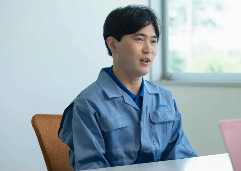 デスクに座り、前を向いて穏やかに話すK.Kさん