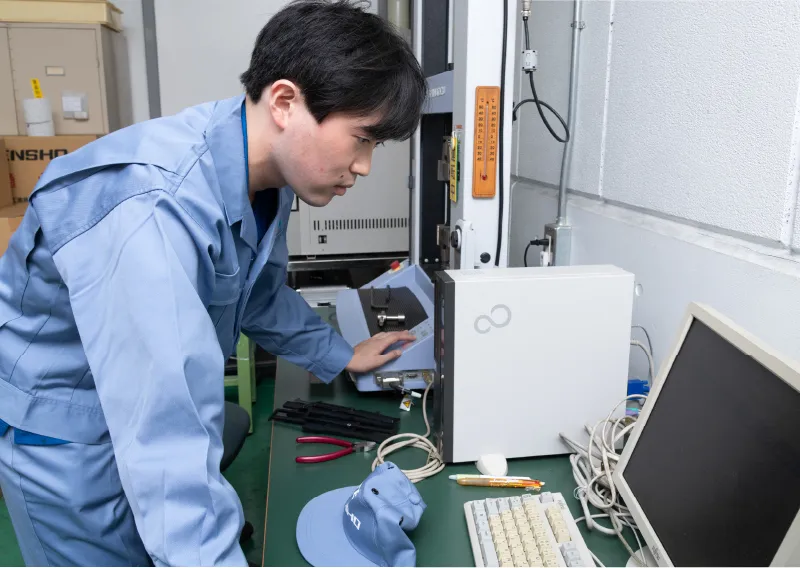 工場内でパソコンに向かいながら、試験機の操作や配線を確認するK.Kさん