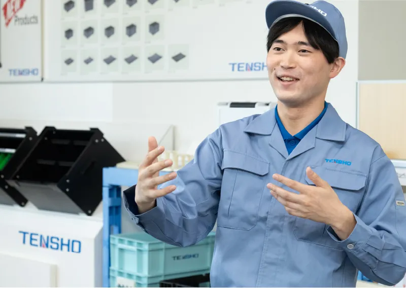 工場内で青い作業服と帽子を着用し、身振り手振りを交えながら笑顔を見せるK.Kさん