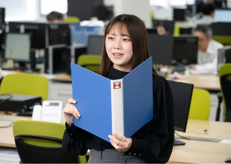 青いファイルを手に笑顔で話す品質保証部／環境管理部のN.Hさん