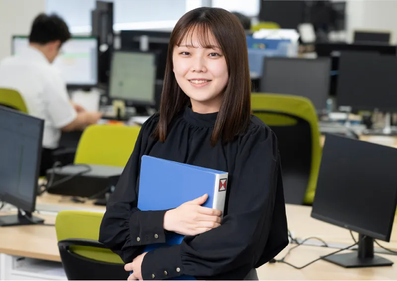 ファイルを抱えて笑顔を見せる品質保証部／環境管理部のN.Hさん