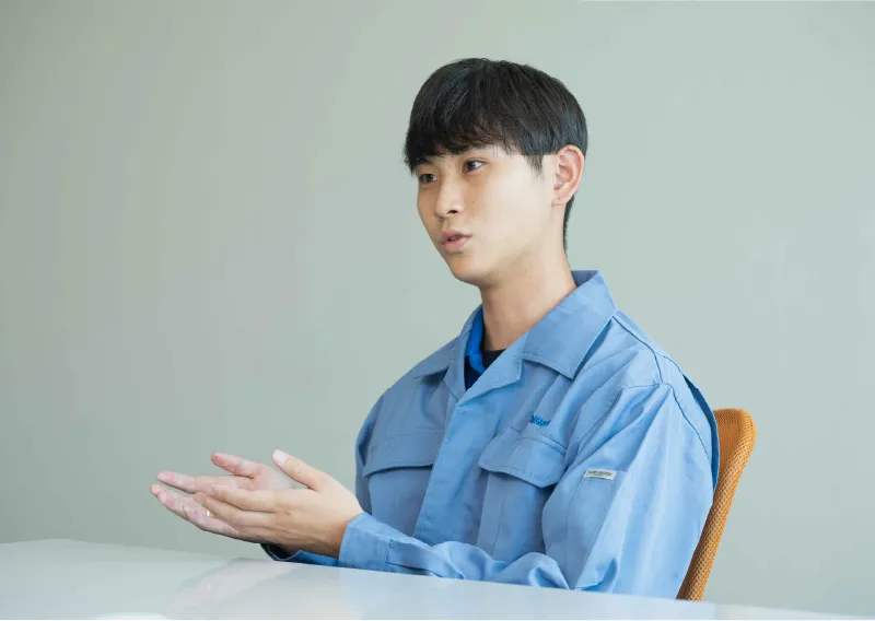 青い作業服を着用し、落ち着いた表情でまっすぐ前を見据えるO.Sさん