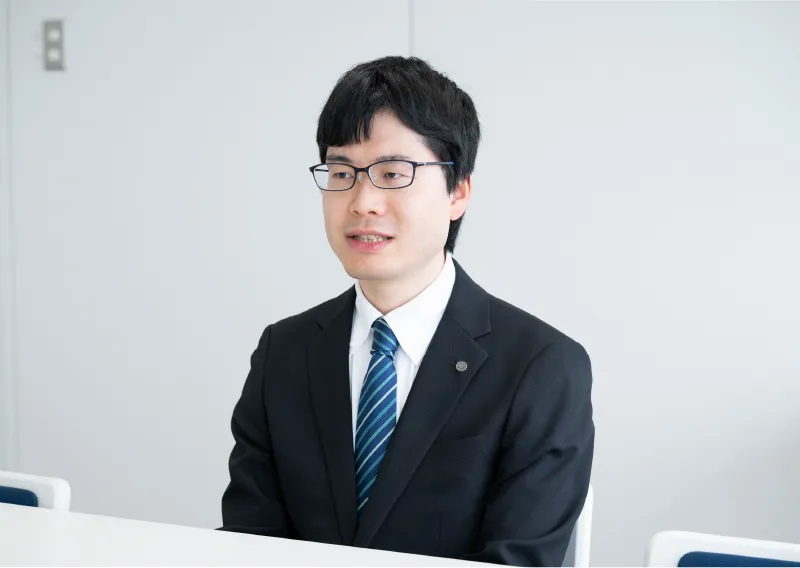 スーツ姿で話を聞く管理本部 購買部のS.Tさん