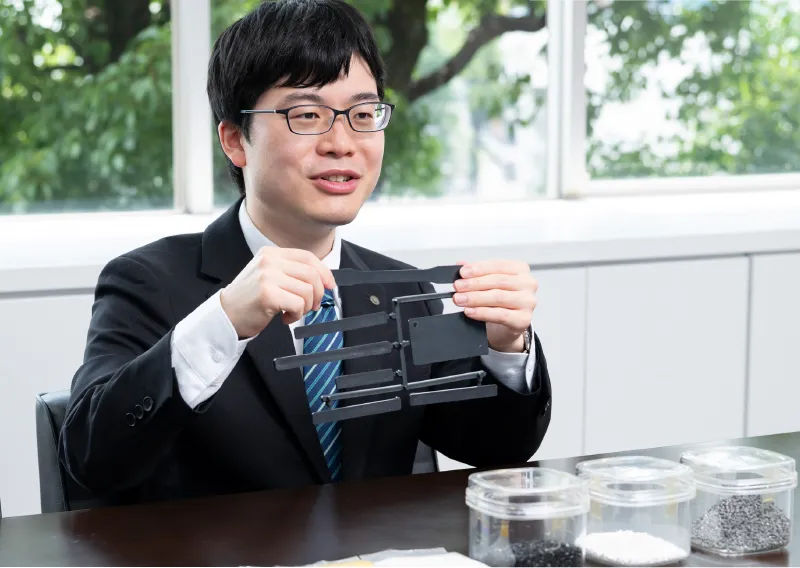 成形品サンプルを手にして笑顔を見せる管理本部 購買部のS.Tさん