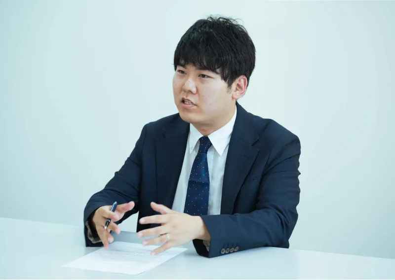 スーツ姿でペンを手に話しをする三重工場 東海近畿営業部のT.Fさん