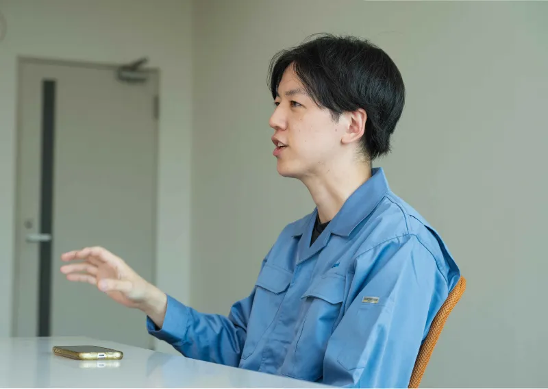 青い作業服を身にまとい、身振り手振りを交えて話すD.Hさん