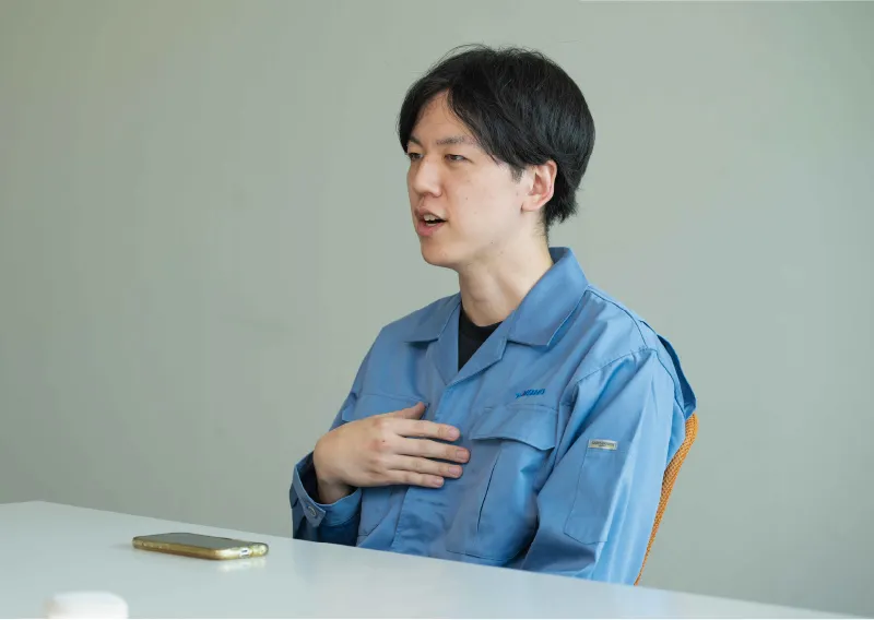 デスクに座り、リラックスした表情で話すD.Hさん