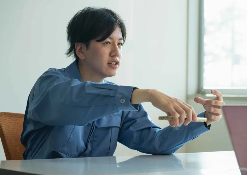 デスクに座り、身振り手振りを交えて笑顔で話すD.Hさん