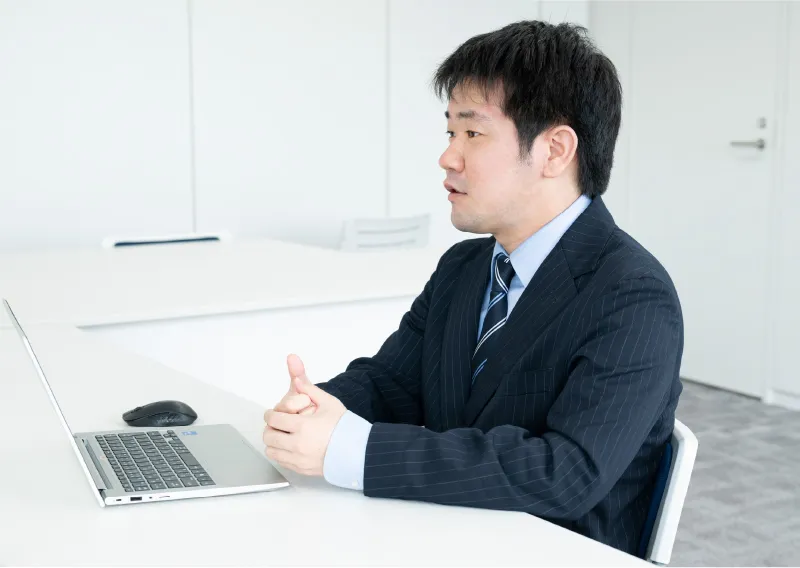 スーツ姿でパソコンに向かい笑顔で話す総務人事部のT.Hさん