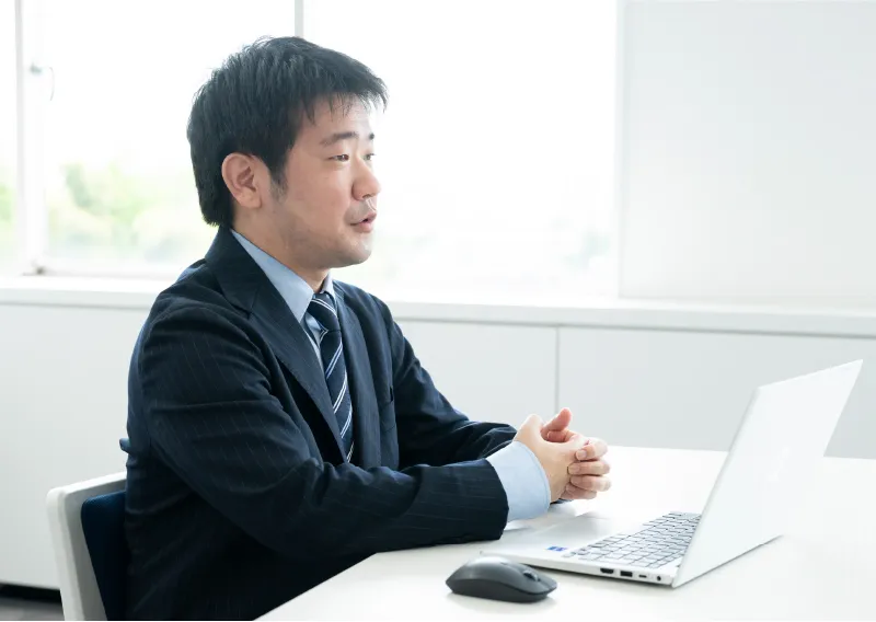 スーツ姿でパソコンに向かい話す総務人事部のT.Hさん