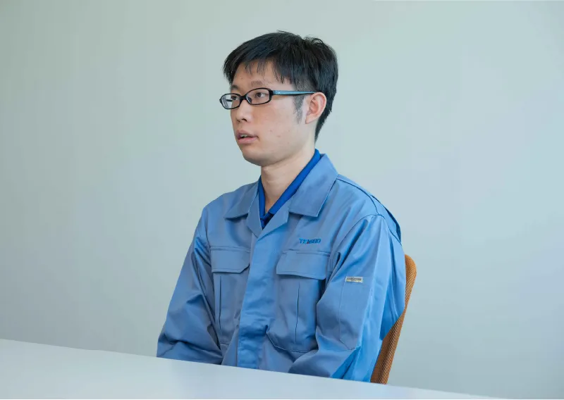 デスクに座り、前を向いて穏やかに話すT.Tさん