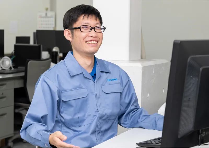 デスクでパソコンに向かい、穏やかな表情で微笑むT.Tさん