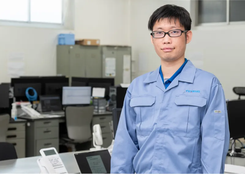 青い作業服と帽子を着用し、真剣な表情でカメラに視線を向けるT.Tさん