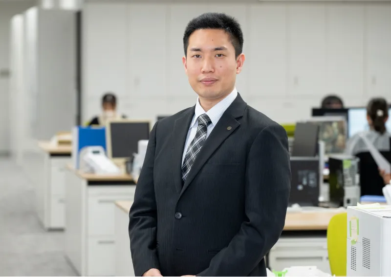 スーツ姿で落ち着いた表情を見せる管理本部 情報管理部のT.Sさん