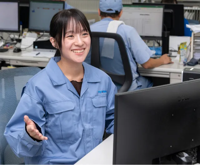作業服姿で笑顔を見せながらパソコン作業を行う工場管理職の社員