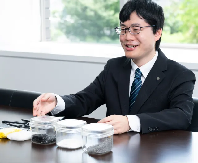 alt="オフィスデスクで原料サンプルを確認しながら業務を行う購買職の社員